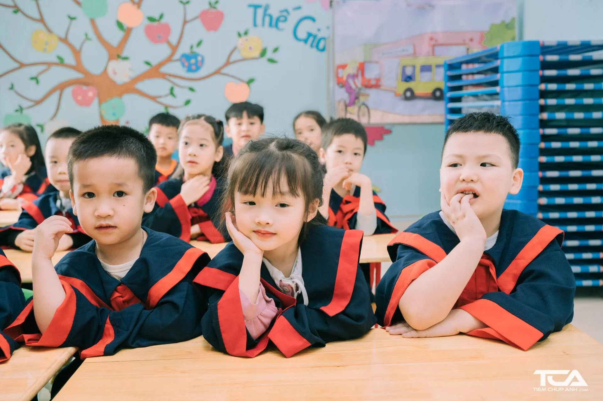 Ảnh các bé mầm non mặc áo cử nhân đang tạo dáng chụp ảnh với khung cảnh ngoài trời
