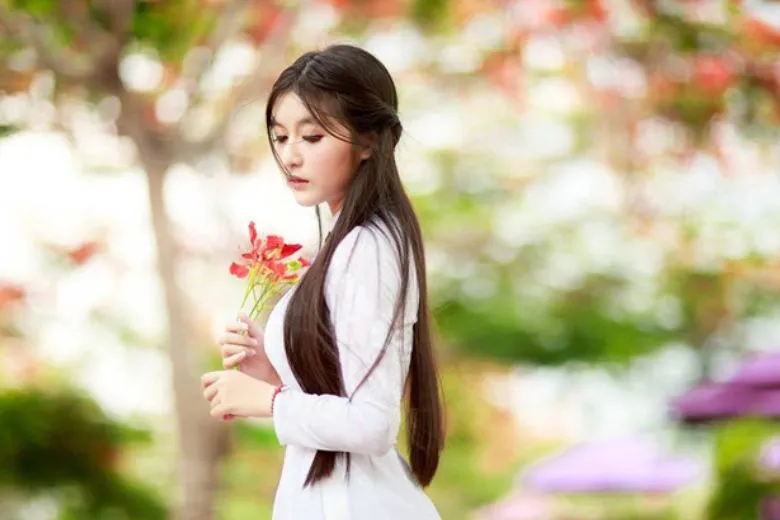 Nữ sinh áo dài trắng tạo dáng nghiêng người với bó hoa hồng đỏ