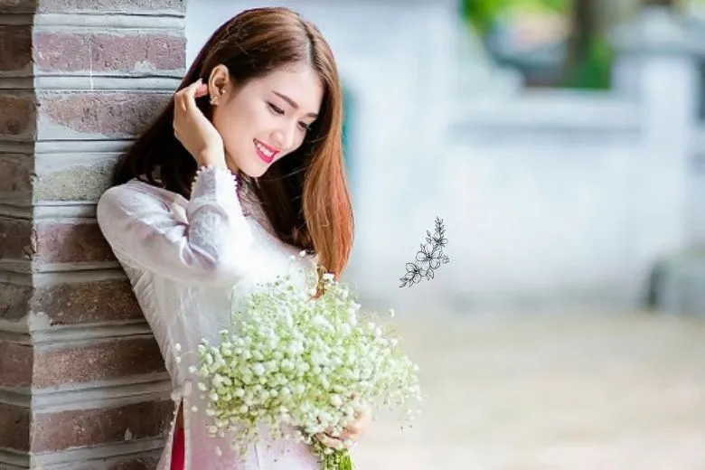 Nữ sinh áo dài trắng cầm bó hoa, tay còn lại vuốt tóc, chụp chính diện