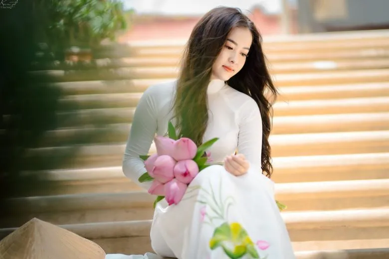 Nữ sinh áo dài trắng đưa bông hoa lên má tạo dáng nhẹ nhàng