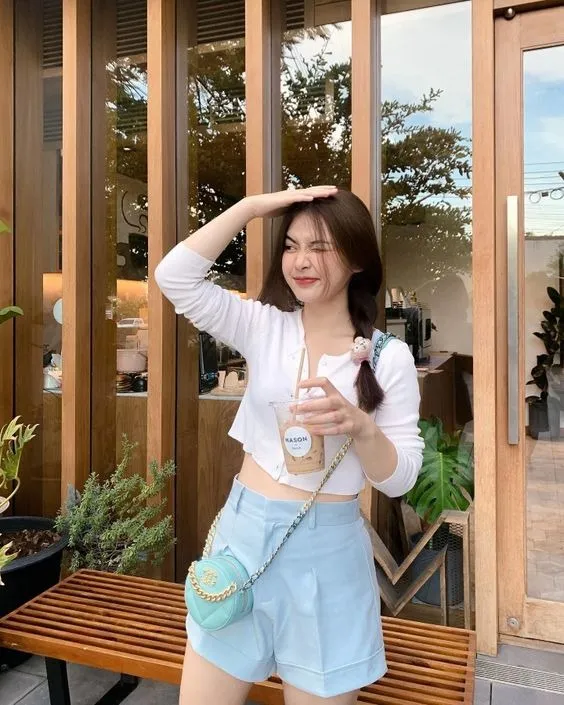 Cô gái đứng cạnh tường gạch cầm ly cafe tạo dáng
